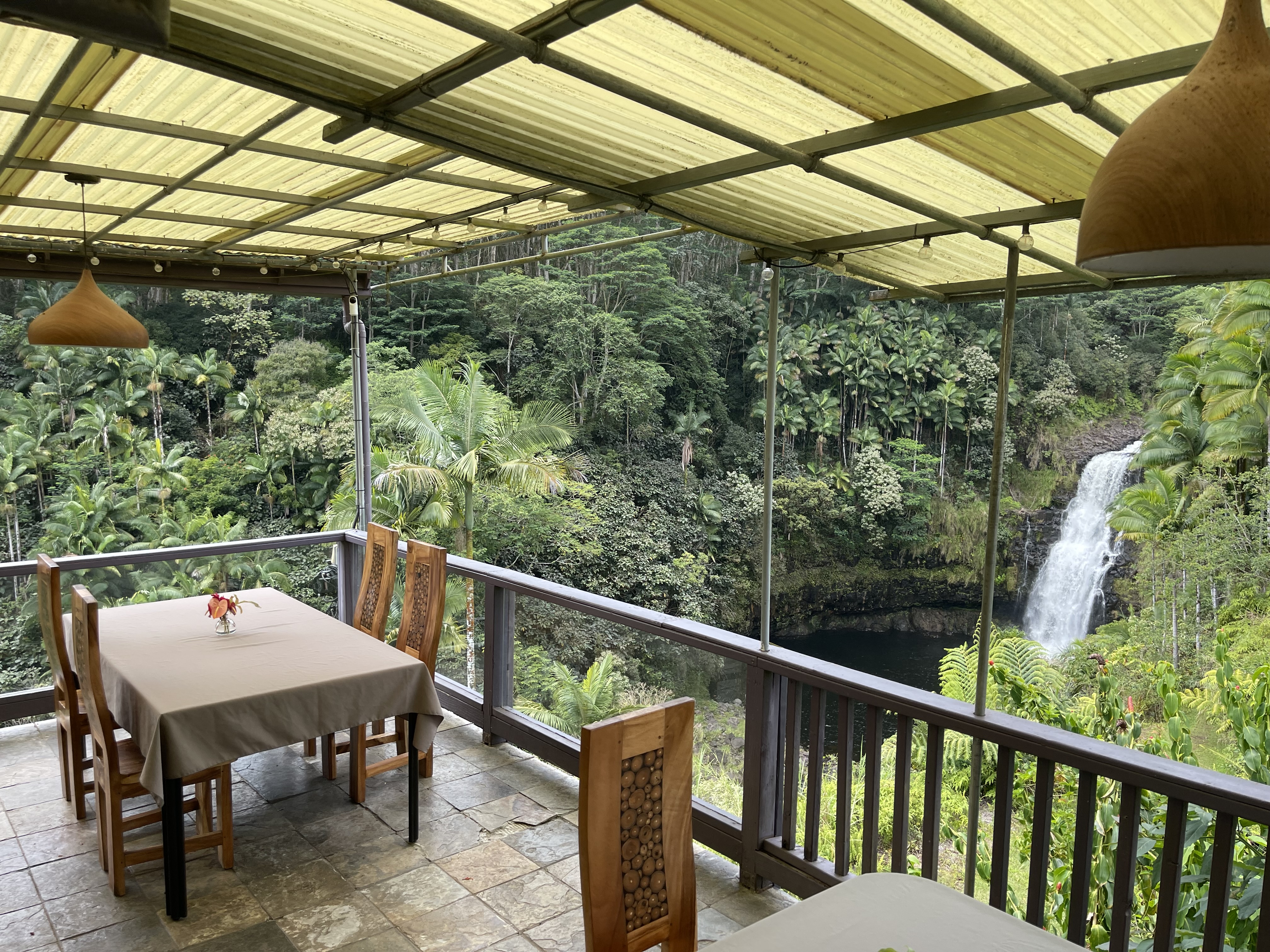 Open-air restaurant lanai overlooking a rainforest waterfall